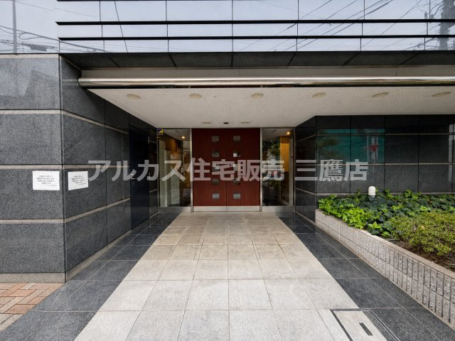重厚感のあるダークグレーの石張り壁とウッド調のドアが印象的なエントランスアプローチ。脇には緑豊かな植栽が配置されています。