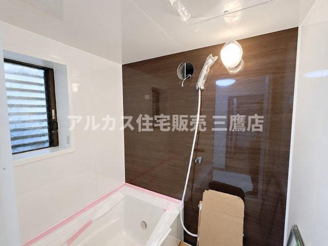 木目調壁面と清潔なホワイトが映えるシステムバス。シャワーヘッドやライトなど洗練された仕様になっています。