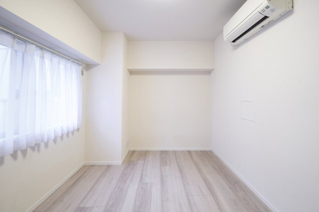 光が差し込む窓とエアコンを備えた、快適に過ごせる洋室。木の質感が心地よいフローリング仕様で、どんな家具とも調和します。入居後すぐに快適な温度設定が可能で、寝室やワークスペースとしても最適です。