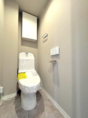 トイレ　清潔感あふれる快適なトイレ空間です。温水洗浄便座などの快適機能を備え、上部にはトイレットペーパーや掃除用品をすっきり収納できる吊戸棚も設置されています。