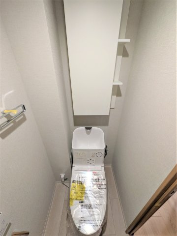白を基調とした清潔感のあるトイレ。上部には収納スペースや棚を備え、トイレットペーパーや日用品をすっきり整理できます。シンプルで使いやすく、毎日気持ちよく利用できる空間です。