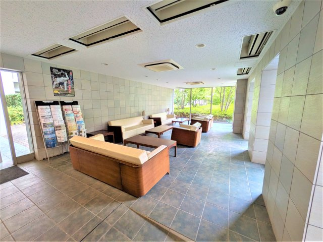大きな窓から緑を望む、明るく開放的なアクアラウンジ。ソファが配置され、くつろぎのひとときを過ごせる共用空間です。