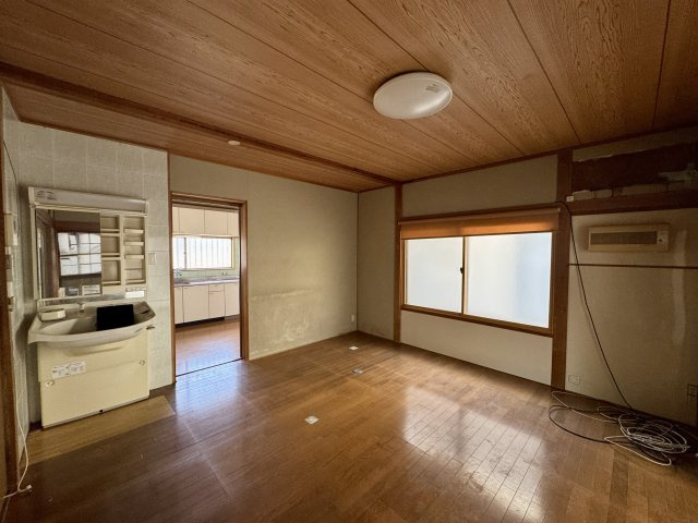 木目調の天井が印象的な温かみのある洋室。広さも十分にあり、リビングとしてもご利用いただけます。大きな窓から自然光が入り、日中は明るく快適な空間に。洗面台やキッチンが近く、生活動線の良さも魅力です。