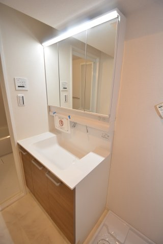落ち着いた木目調が映える洗面空間。三面鏡収納と広い鏡で身支度快適、浴室と統一感ある一室です。