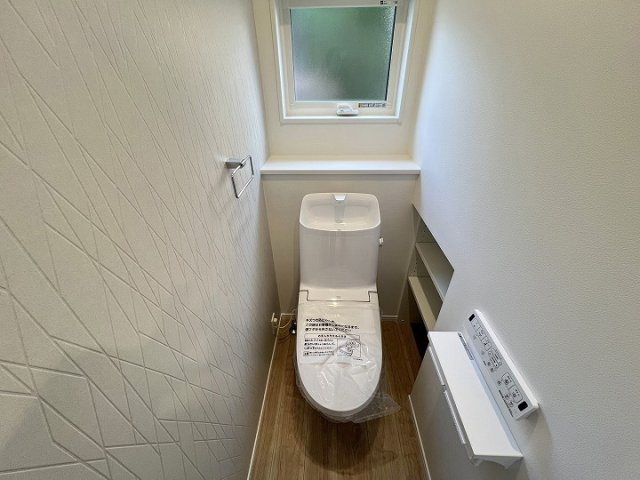 幾何学調のアクセントクロスがお洒落な温水洗浄機能付きトイレです。　自然光が差し込む小窓が配置されており、手軽に換気が行える設計となっています。