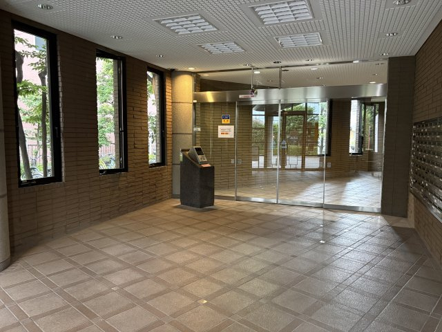 防犯面に配慮された安心のオートロックシステムを搭載。縦長の窓から柔らかな自然光が差し込むロビーは、タイル貼りの床や壁面が気品ある空間を演出します。右側には整然と並ぶメールボックスも配置されています。