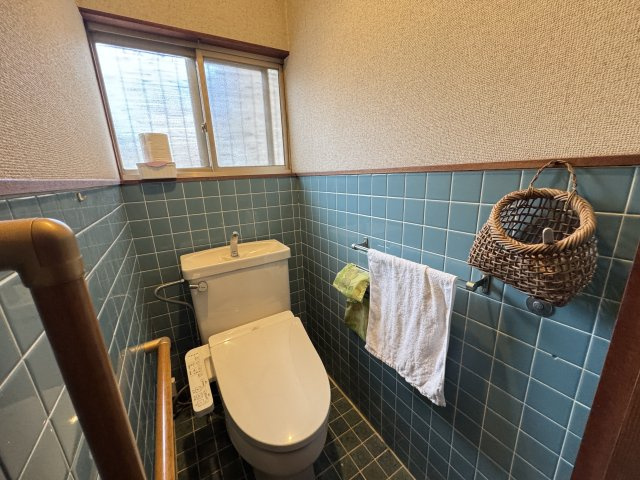 温水洗浄便座付きで快適に利用できるトイレ空間。窓付きで換気がしやすく明るさも確保されています。手すりが設置されており安全面にも配慮。落ち着いたタイル仕上げが印象的で、清潔感のある使いやすいトイレです。