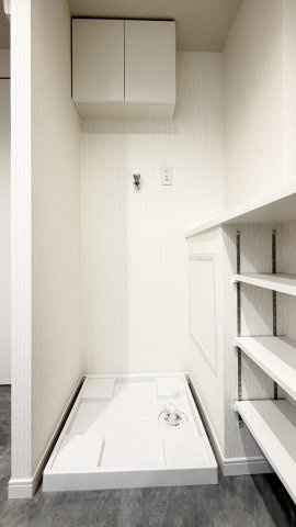 【室内洗濯機置き場】　上部に吊戸棚、横に棚を備えた洗濯機置き場。洗剤やタオルを手元に置けて家事が楽になります。