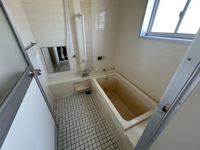 手すりや給湯リモコンが設置された、窓付きのバスルーム。