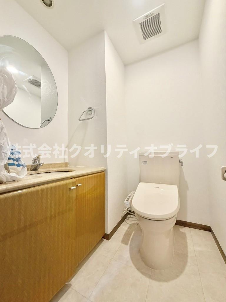 木目調キャビネットと上品な丸鏡が優雅な趣を演出するトイレ空間。独立した手洗いカウンターを完備しており、来客時のゲスト用としても気兼ねなくお使いいただける高品位な設えで
