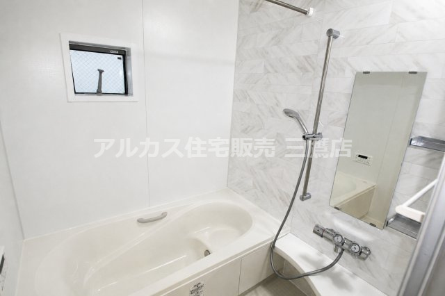 大理石調のアクセント壁と小窓を備えた浴室。棚付きでバス用品も整理しやすい空間です。