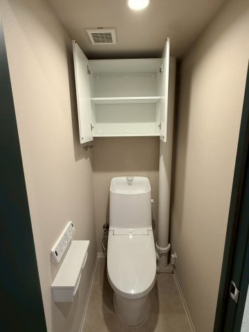 温水洗浄機能付きトイレと扉付き上部収納を備えた機能的な空間です