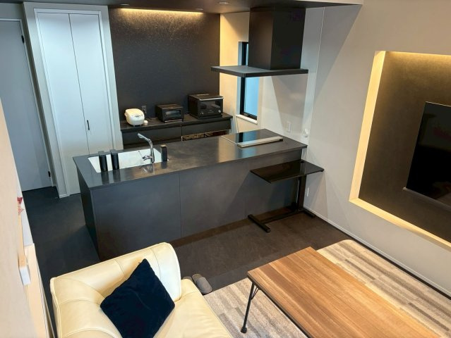 天井高のある開放的な空間に映えるスタイリッシュなブラックのアイランドキッチン。広々としたカウンターで料理や配膳がしやすいです。高級感と機能性を兼ね備えたデザインで、上質なキッチンスペースです。