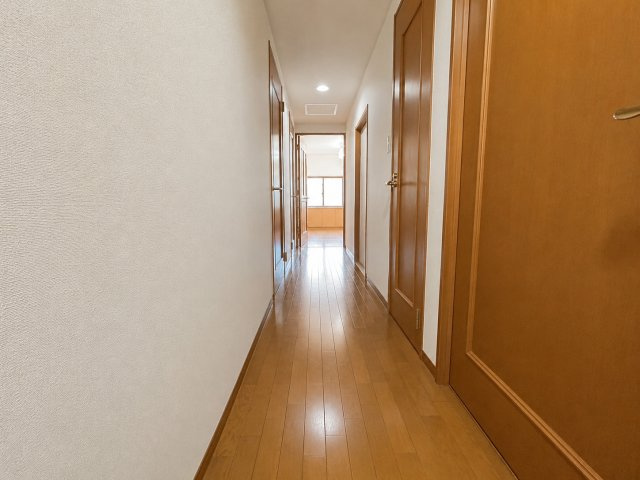 木目調のフローリングと建具で統一された、温かみのある廊下スペース。奥まで見通せるすっきりとした動線で、各居室や水回りへ移動しやすい間取りです。白を基調とした壁面が明るく清潔感のある印象を与えています。