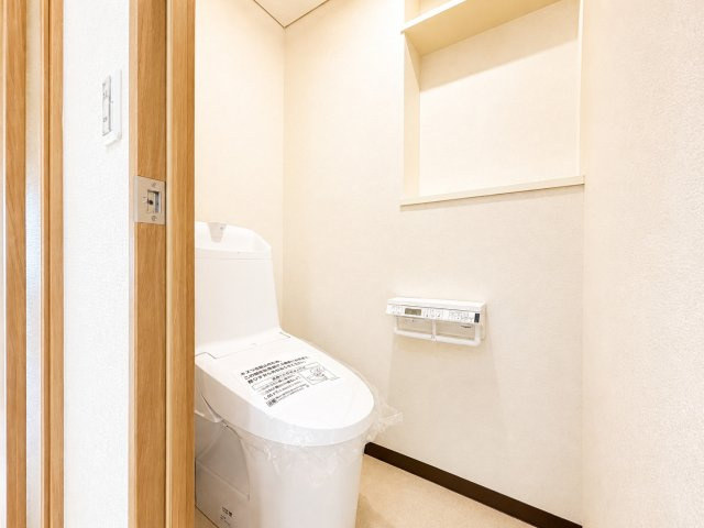 落ち着いた雰囲気のトイレ空間です。温水洗浄便座付きで、快適に使用できます。操作パネルはペーパーホルダーについており、見た目もすっきりします。清潔感があり、毎日気持ちよく使える仕様です。