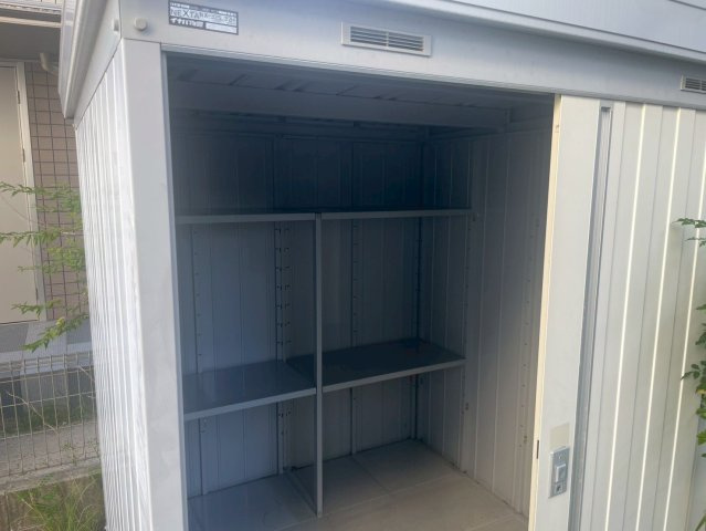庭に設置されたスチール製の収納コンテナです。広々とした内部には可動式の棚が備わり、園芸用品やアウトドアグッズ、工具などを効率的に整理・保管できます。スライド式扉で開閉がスムーズで耐久性にも優れています