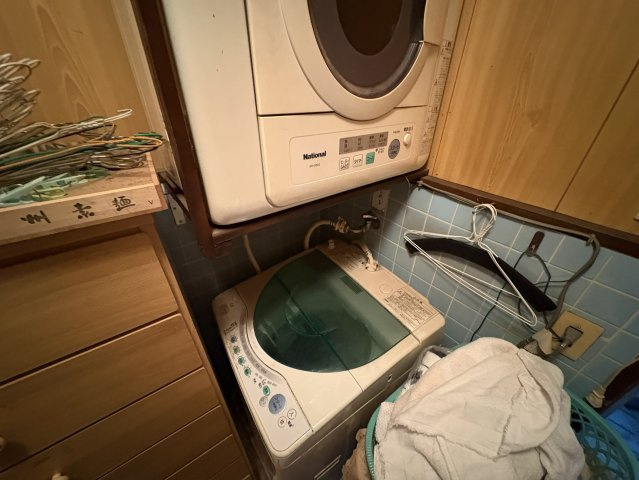 洗濯機置場と乾燥機スペースがまとまった実用的な洗濯スペース。上下に配置できるため、省スペースながら洗濯から乾燥までの作業がスムーズ。周辺には収納家具や物干し用ハンガーを掛けられる工夫もあります。