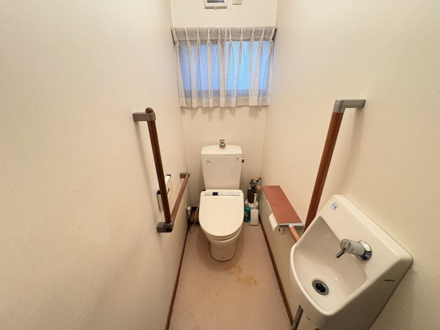 手すりを備えたトイレ空間で、立ち座りの動作をサポートする配慮のある造り。窓付きのため自然光が入り、換気もしやすく清潔感を保ちやすい点が魅力。手洗い器も設置されており、使用後すぐに手洗いができる実用的。