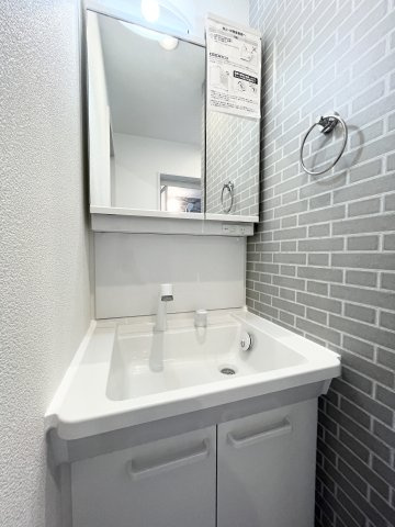 白を基調とした清潔感のある洗面化粧台。鏡横のアクセントクロスが空間におしゃれな印象を添えています。