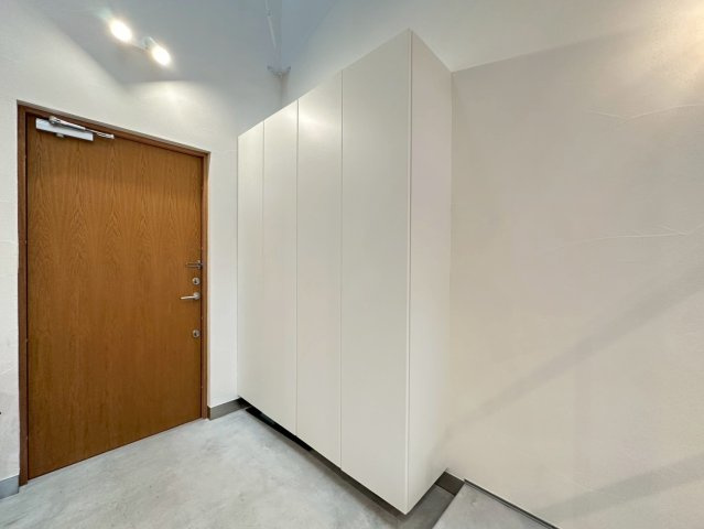 白を基調とした清潔感のある空間で、大型の壁面収納（シューズボックス）が設置されています。玄関ドアは外観のアクセントにもなっている温かみのある木目調のデザインです。