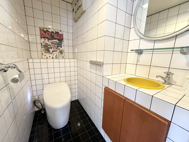 スタイリッシュな白タイルと黒床のコントラストが美しいトイレ空間。最新のタンクレス仕様で、スッキリとした印象に。黄色の洗面ボウルがアクセントとなり、遊び心のあるインテリアが魅力です。