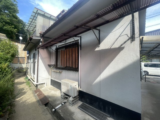 建物側面には通路が確保され、窓には格子や庇が設けられています。給排水設備やエアコンの室外機なども確認できます。建物まわりには通路が確保されており、外周の様子や隣接する建物との距離感なども確認できます。