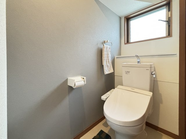 落ち着いた色合いのクロスが印象的なトイレは窓付きで自然光と換気がしっかり確保された快適な空間です。温水洗浄便座を備え毎日使う場所としての使い勝手も良好。スリムな空間ながら清潔感があり気持ちよく使えます