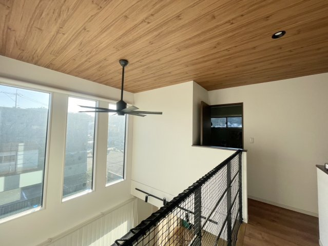 大きな連窓から自然光がたっぷりと入る明るい2階ホール。木目天井とブラックのファンがデザイン性を高め、ホテルライクな雰囲気を演出。吹き抜けを見下ろせる位置にあり、家族の声が届きやすい一体感ある空間。