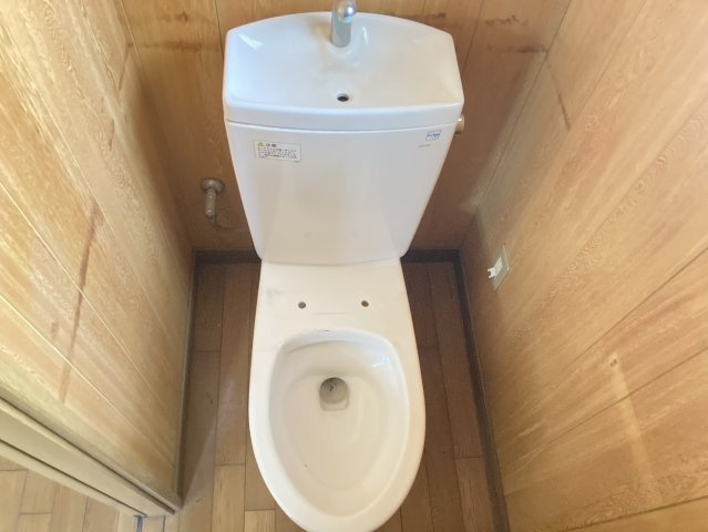 木目調の壁に囲まれた、落ち着きのあるトイレスペース。便器には手洗いが一体となっており、限られた空間を効率よく活用しています。シンプルな造りで、お好みに合わせて便座や内装をリフォームする楽しみもあります