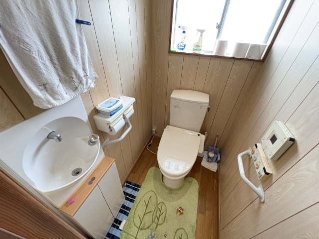 温水洗浄便座付きのトイレは、手すりも設置されており高齢の方にも配慮された仕様。小型手洗いスペースや窓付きで清潔感もあり、明るく快適に使用できます。室内には壁リモコンも完備しています。