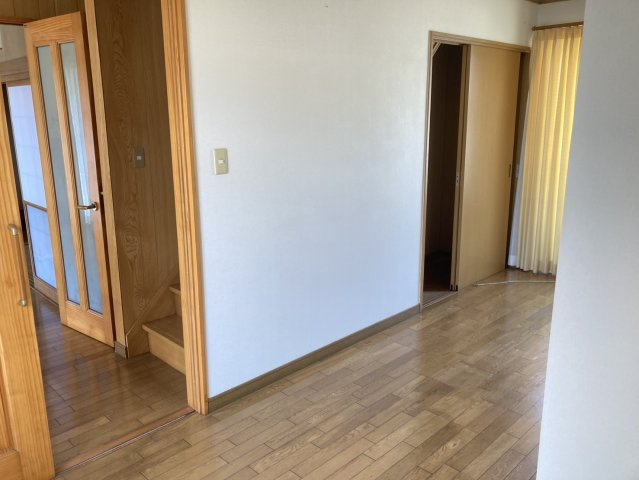 明るい色合いの壁と木目のフローリングが調和した、温かみのある洋室です。窓から自然光が差し込み、室内を明るく演出。隣接する空間や廊下への動線も確保されており、生活しやすい間取りです。