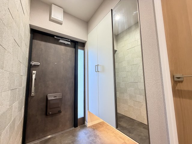 シックなドアと重厚感漂うタイル調壁面が調和する玄関ホール。足元をすっきり見せるフロートタイプの収納と全身鏡を備え、毎日の出入りをスマートかつ快適にサポートします。　