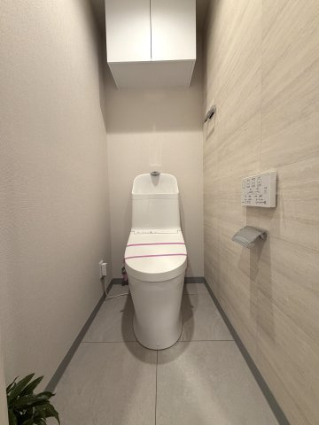 トイレ上部には扉付きの吊戸棚を設置。生活感を隠しながら予備のトイレットペーパーや掃除用品をスマートに収納できます。便利な壁付けリモコン付きで操作もスムーズです。