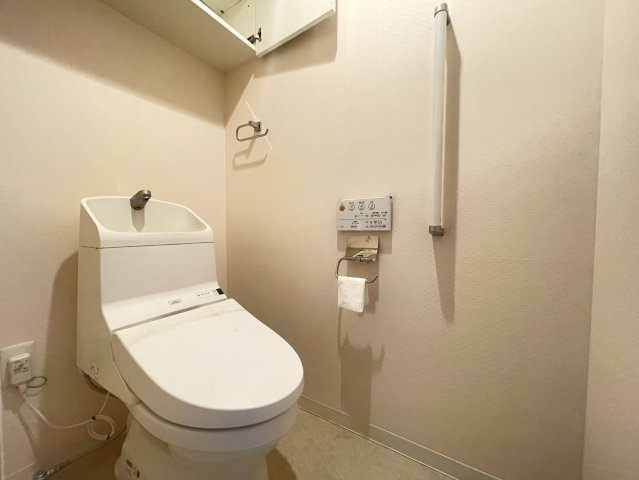 温水洗浄便座付きの清潔感あるトイレ空間。上部には収納棚が設けられており、トイレットペーパーや掃除用品の収納に便利です。手すりも設置されているため立ち座りも安心。シンプルで使いやすいレイアウト。