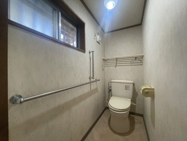 ゆとりある広さのトイレ空間。手すりが設置されており、立ち座りも安心して行えます。窓付きで自然換気ができ、明るさも確保。上部には棚もあり、トイレットペーパーなどのストック収納にも便利です。