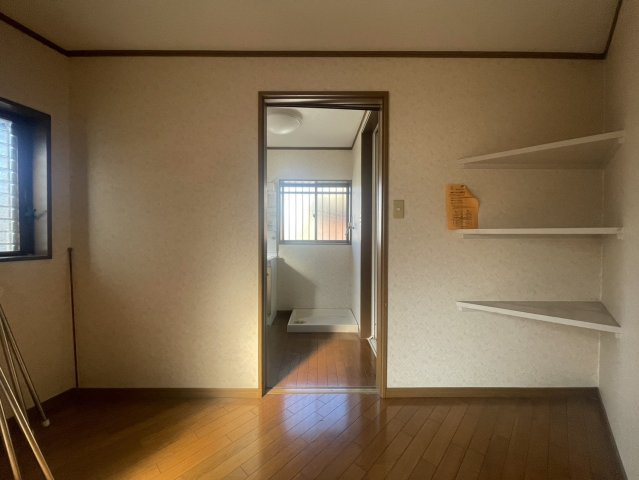 落ち着いた色合いのフローリングが印象的な洋室スペース。窓からやわらかな光が差し込み、明るく心地よい空間です。隣室へとつながる動線もスムーズで、家事や身支度も効率的。壁面には使い勝手の良い可動棚を設置。