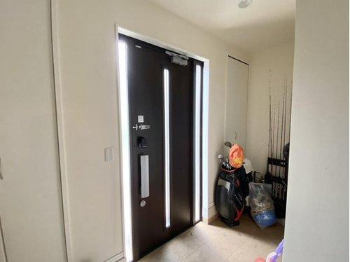 ダークブラウンの玄関ドアが空間を引き締めるスタイリッシュな玄関。サイドに縦長の窓があり、自然光を取り込みつつプライバシーも確保。奥には収納スペースもあり、実用性も◎。