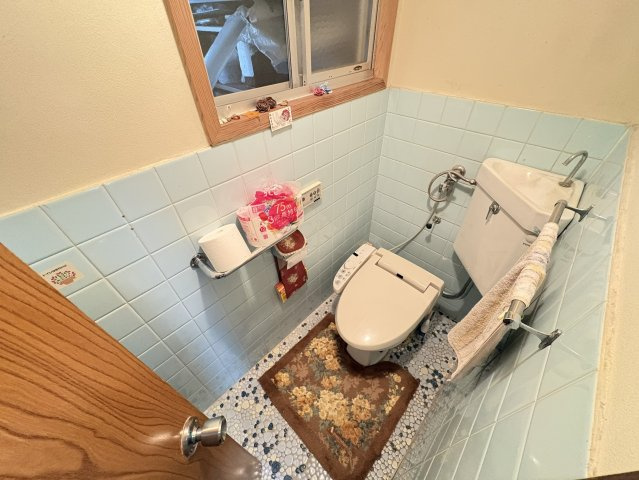 水色のタイルが爽やかな印象を与えるトイレは、窓付きで換気性が高く、清潔感を保ちやすい空間です。温水洗浄便座を備え、日常的な使いやすさも配慮されています。手洗いやタオル掛けも整っており、快適な仕様。