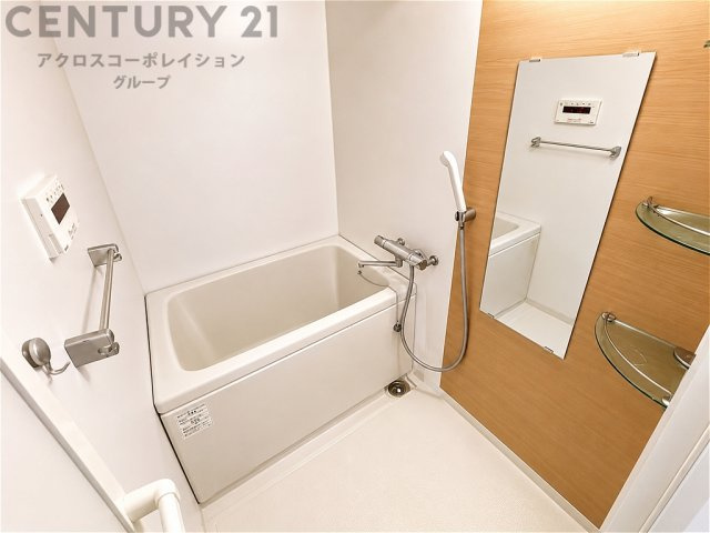 明るく清潔感あふれるバスルーム。木目調のアクセントパネルが温かみを演出します。大きな鏡や収納棚も備え、毎日のバスタイムを快適に過ごせる空間です。