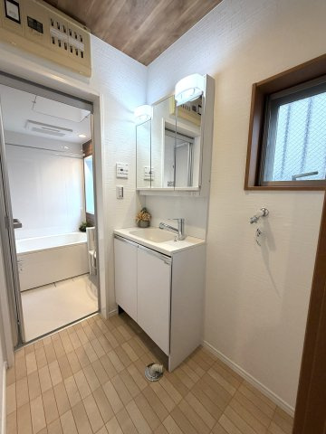 白を基調とした明るく清潔感あふれる洗面室。小窓付きで自然な光が差し込み、毎日の身支度も心地よく行えます。鏡裏収納を備えた三面鏡タイプの洗面化粧台で、洗面周りもすっきり整います。