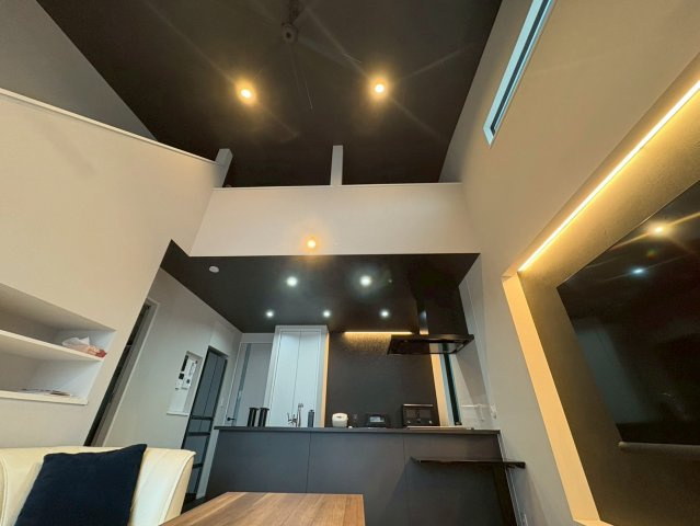 天井高の吹き抜けが開放感を生み出す、明るくゆとりあるリビング。高窓から自然光が差し込み、昼間は照明いらずの心地よい空間です。ブラックを基調としたキッチンが空間を引き締め、デザイン性と機能性を両立。