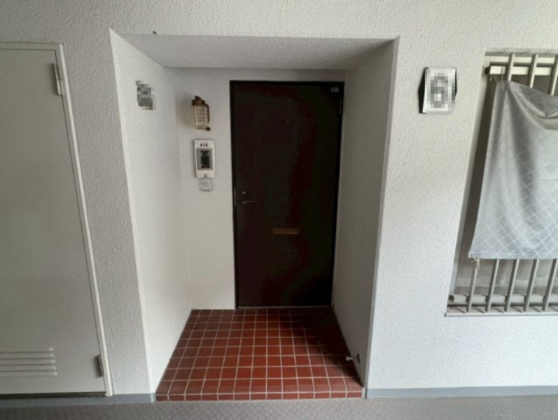 玄関前の共用部分は、ゆとりあるスペースが確保されており、荷物の出し入れもしやすい造りです。床は滑りにくいタイル仕上げで、雨の日も安心です。住戸番号プレートや照明が整備され、清潔感のある印象を与えます。