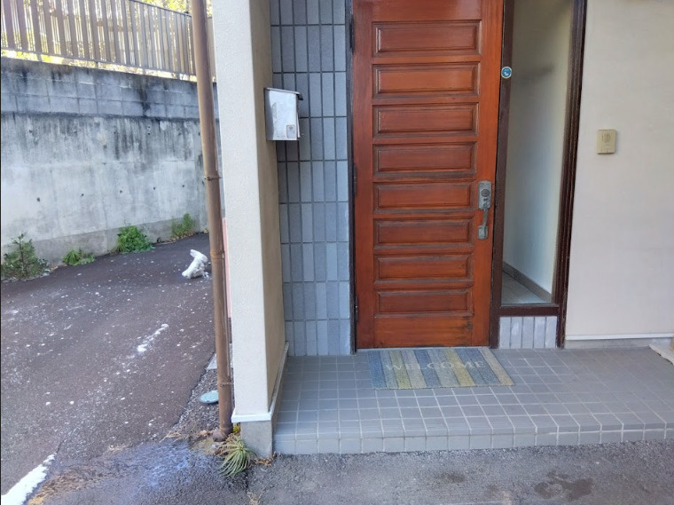 温かみのある木目調の玄関ドアが印象的なエントランスです。　屋根付きのポーチ仕様となっており、雨の日でも落ち着いて鍵の開閉が可能です。タイル張りの玄関まわりはお手入れもしやすく、清潔感を保てます。