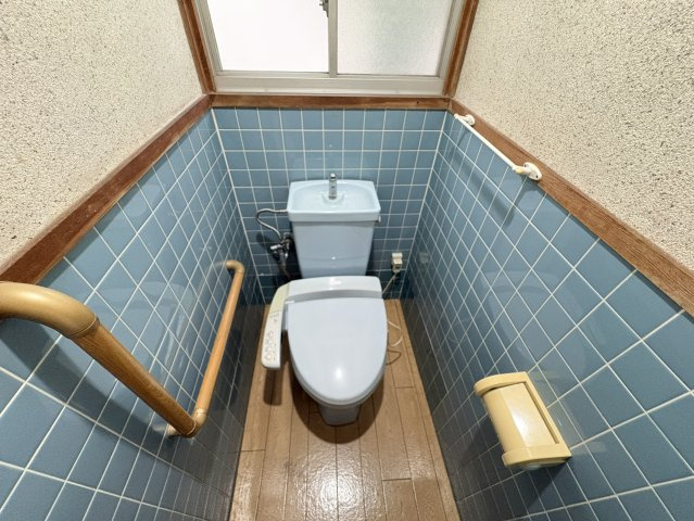 落ち着いた色合いのタイルが空間のアクセントになっているトイレ。温水洗浄便座付きのため、毎日快適にご利用いただけます。手すりを設置しているため、小さなお子様やご年配の方にも配慮された設計となっています。