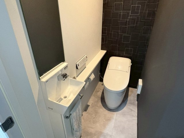 落ち着いた色調でまとめられたモダンなトイレ空間。手洗いカウンター付きで衛生的に使え、背面のアクセントクロスが上品な雰囲気を演出します。清潔感とデザイン性を兼ね備えた心地よい空間に仕上がっています。