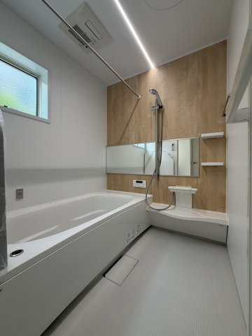 木の温もりを感じるナチュラルなアクセントパネルがお洒落な浴室。空間を広く見せるワイドミラーや、天井をすっきり照らす先進的なライン照明を採用。便利な浴室換気乾燥機も完備しています。
