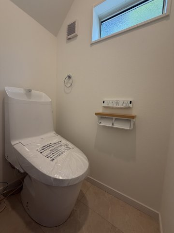 清潔感あふれる明るいトイレスペース。スマートな壁掛けリモコン付きの温水洗浄便座を採用。スマートフォンやちょっとした小物を置くのに重宝する、お洒落な木目調カウンター付きです。