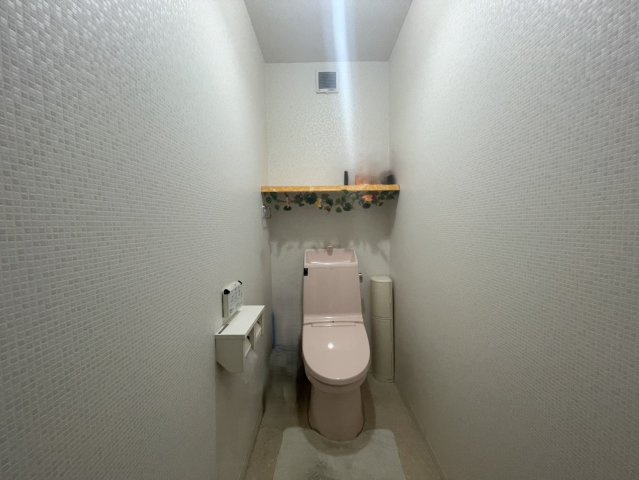 壁面に棚を備えたすっきりとしたトイレ空間。やわらかな色合いで落ち着いた雰囲気に仕上がっています。上部棚は小物やストックの収納に便利で、空間を有効活用可能。清潔感を保ちやすい設計です。