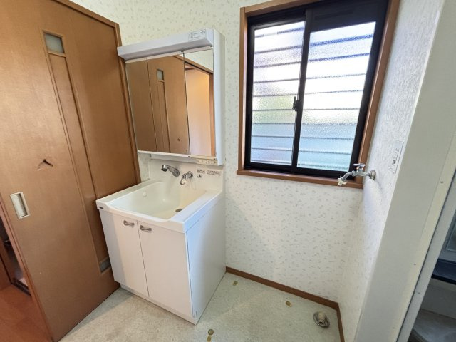 三面鏡の洗面化粧台は収納力が高く、洗面用品や小物類をすっきり整理できます。窓付きで換気しやすく、朝の支度や家事がスムーズに行える機能的な空間。洗濯機置き場も近く、生活動線が整った使いやすい洗面所です