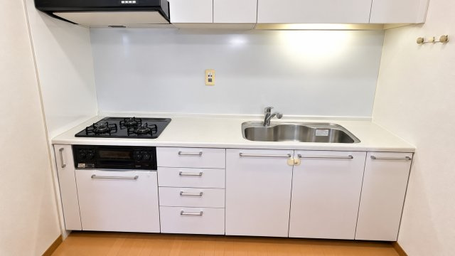 清潔感のあるホワイトカラーでまとめられたシステムキッチン。3口ガスコンロを備えており、複数の料理を同時に進めやすい仕様です。上下に収納スペースが充実し、調理器具や食器類もすっきり整理可能。